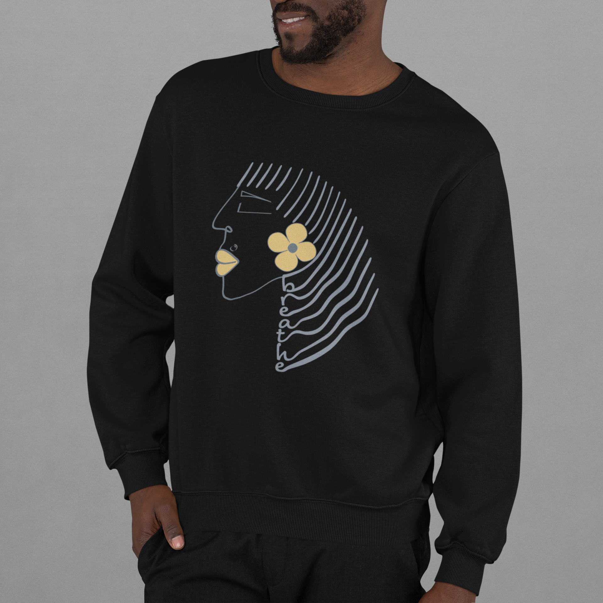 Black crewneck sweatshirt with minimalist Breathe graphic, featuring abstract face line art, yellow flower, and text along flowing hair lines. Positive and motivational graphic tees.
