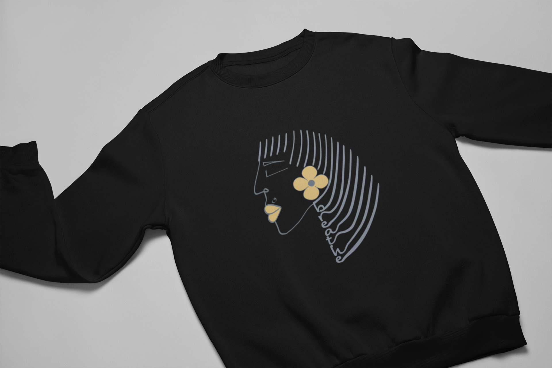 Black crewneck sweatshirt with minimalist Breathe graphic, featuring abstract face line art, yellow flower, and text along flowing hair lines. Positive and motivational graphic tees.