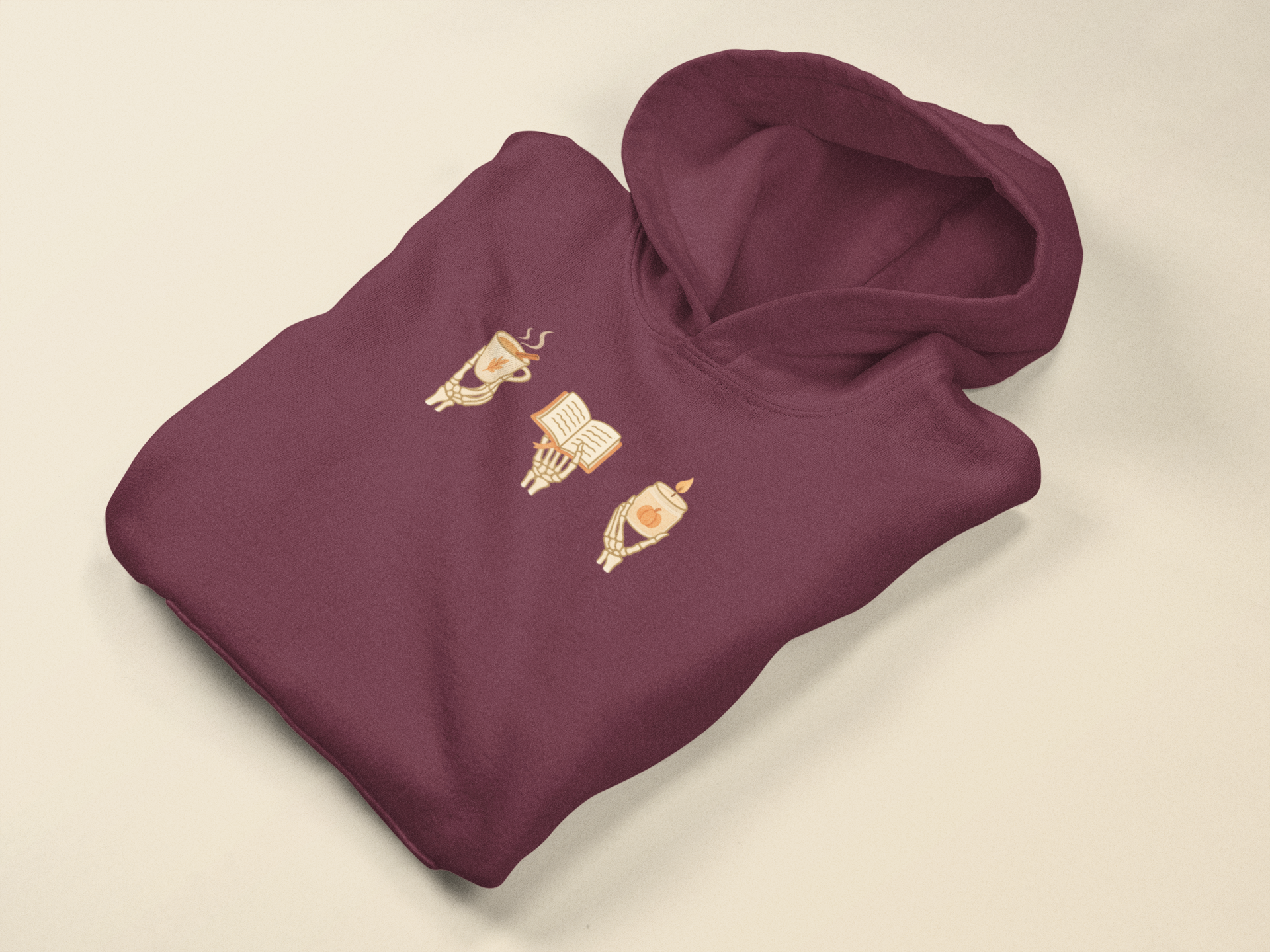 Adult hoodie in maroon with 'Cozy Bones' graphic print. Fall & halloween themed graphic sweatshirts. 