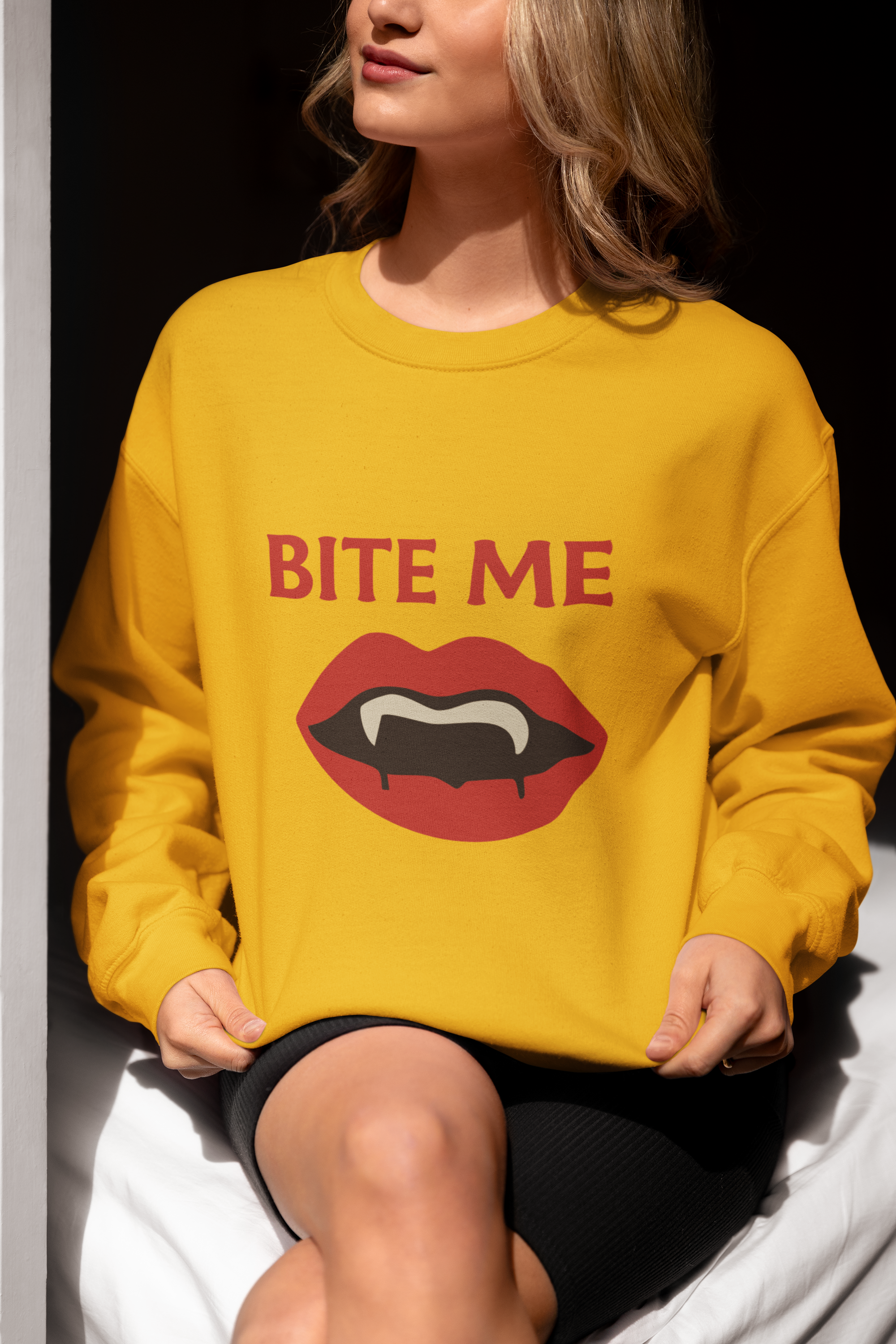Adult sweatshirt in gold with 'Bite Me' graphic print with vampire fangs. Funny halloween themed graphic tees. 